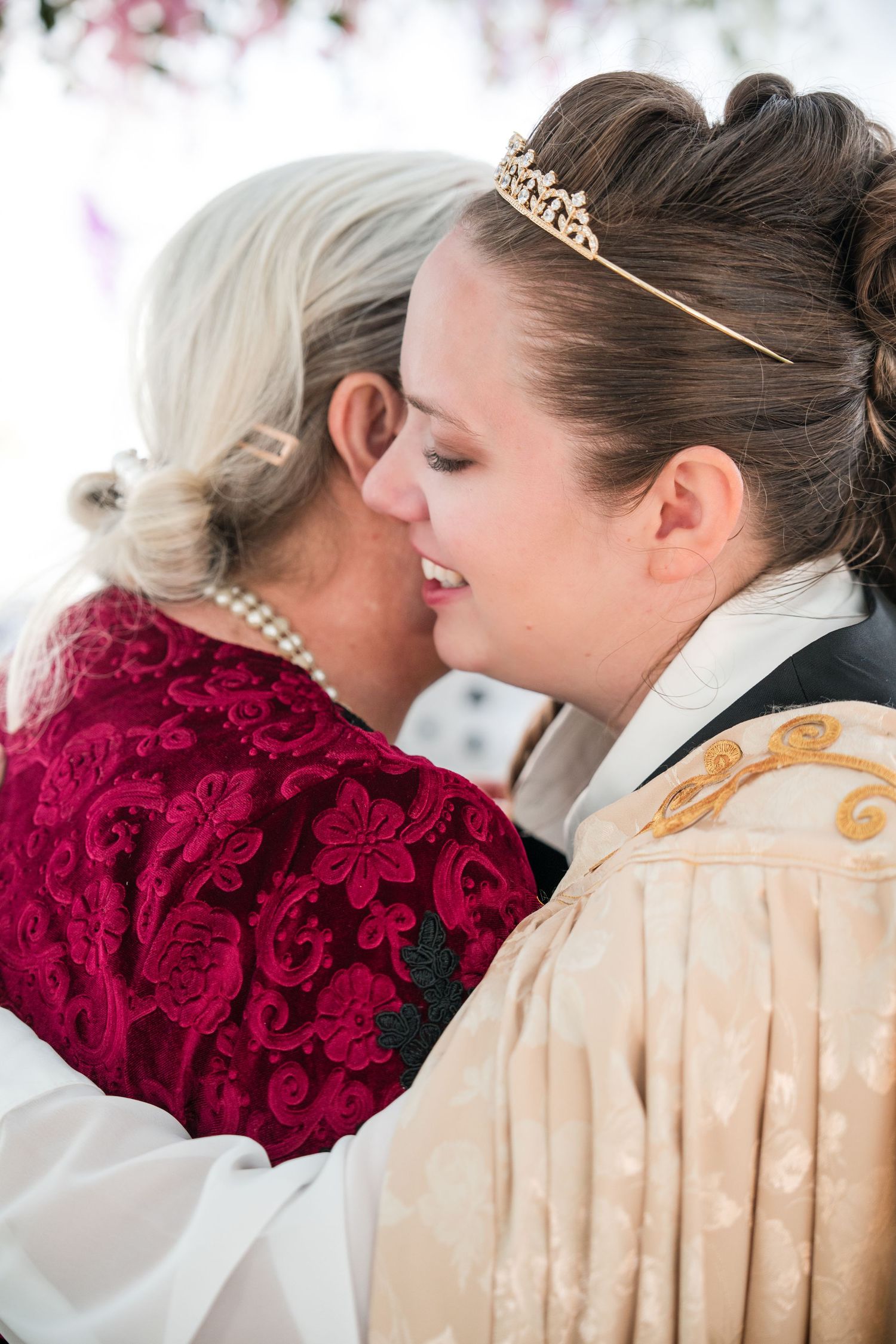Two people in formal attire embrace while holding a bouquet of deep red roses at a wedding ceremony.