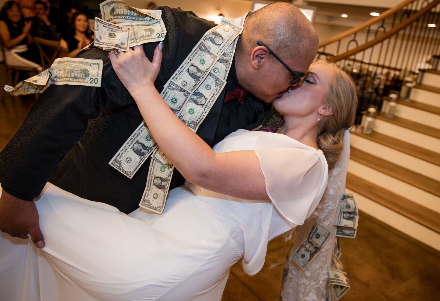 Couple in wedding attire shares romantic dance dips in front of a grand staircase at their reception.