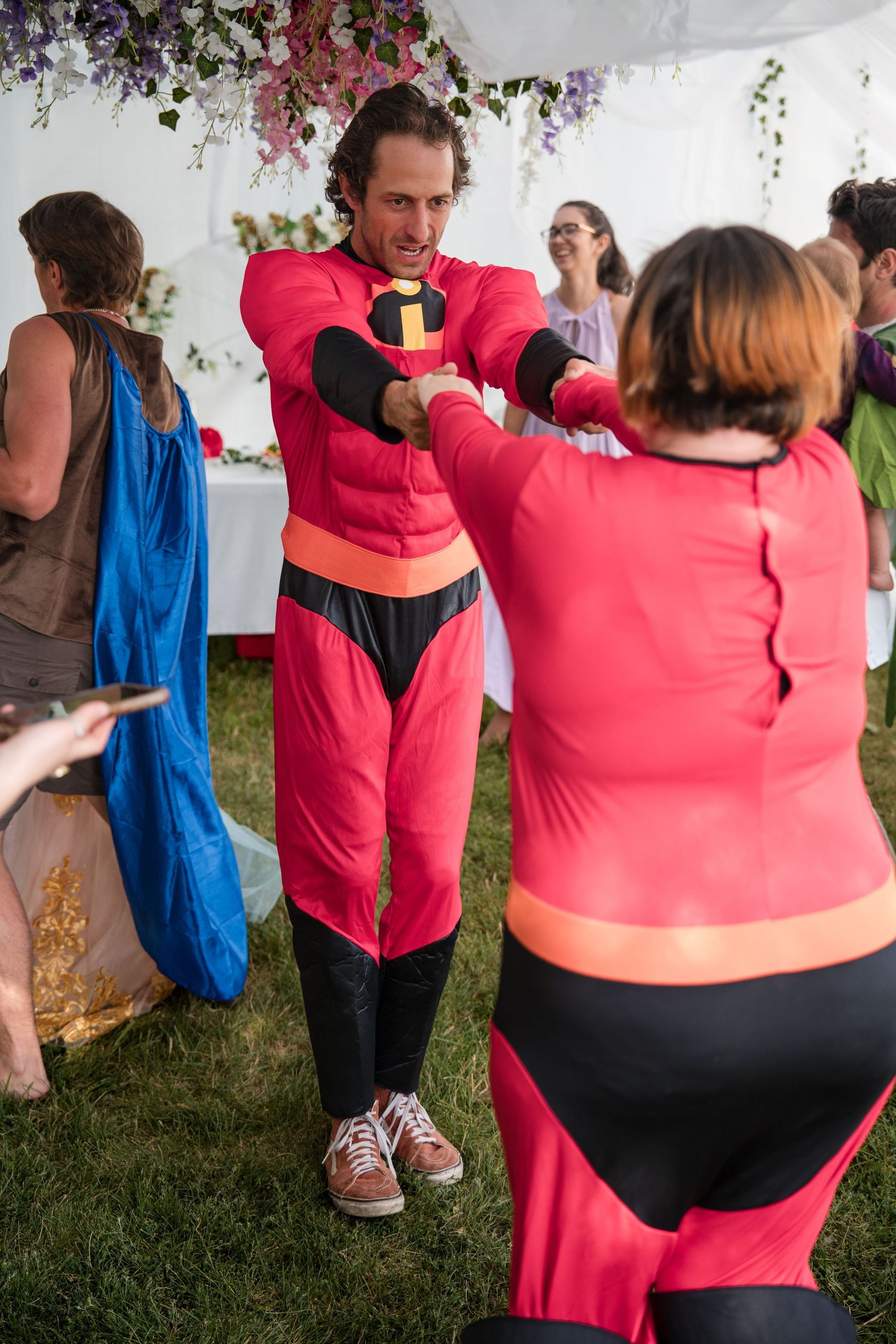 Two people in bright red and black athletic outfits practice dance or exercise moves under a tent with floral decorations.