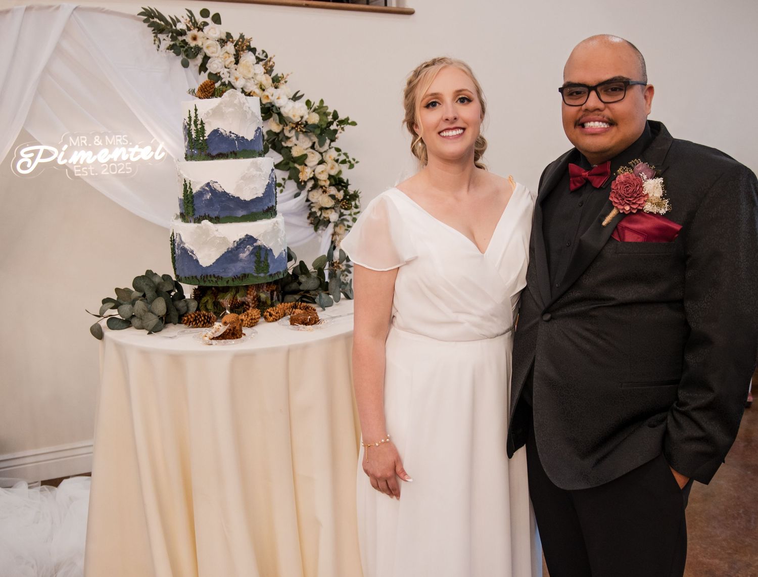 A three-tiered navy and white wedding cake decorated with eucalyptus stands on display at an elegant reception.