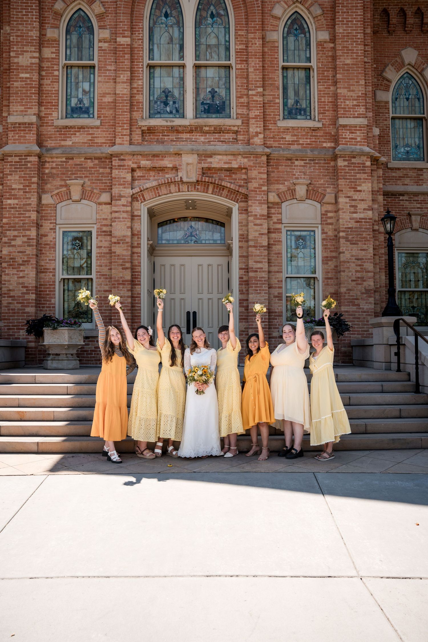 Wedding party in yellow and orange dresses poses on steps of the Provo City Center LDS temple with Gothic architecture details.