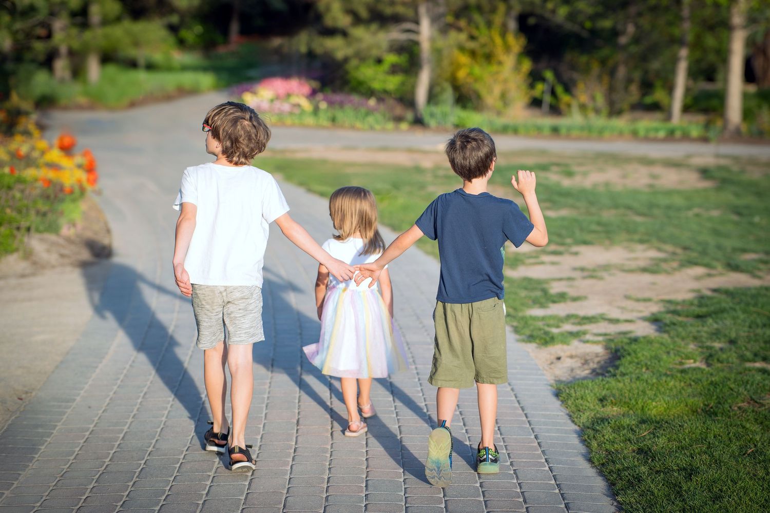 Children walking together hand in hand along a garden path on a sunny afternoon.