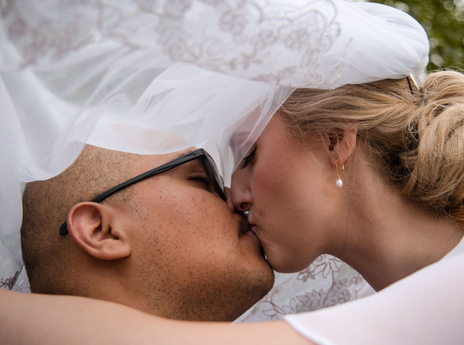 A couple wearing light colored clothing share a romantic kiss in front of a pastel background.