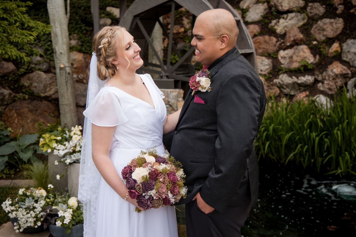 Wedding couple poses together in an outdoor garden setting with stone walls and lush greenery in a collection of portraits.