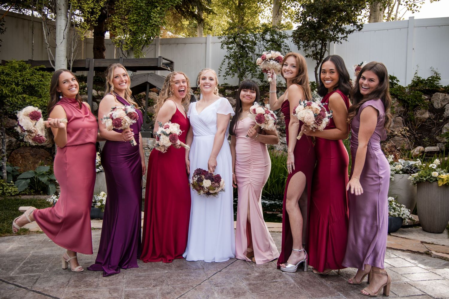 A wedding party wearing coordinated pink and purple dresses stands together in a sequence of outdoor photos.