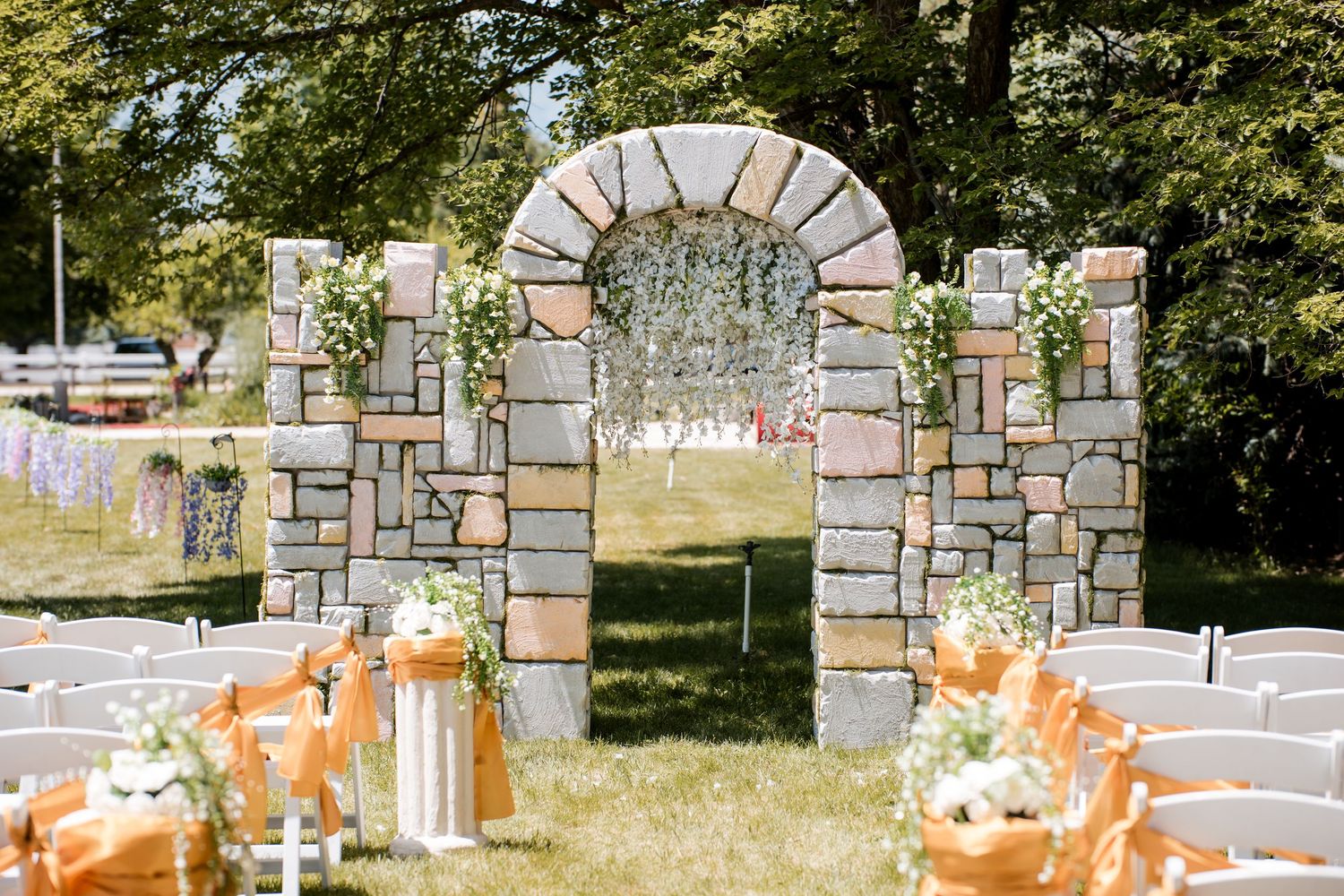 Stone wedding arch decorated with lanterns and orange floral arrangements in an outdoor garden setting.