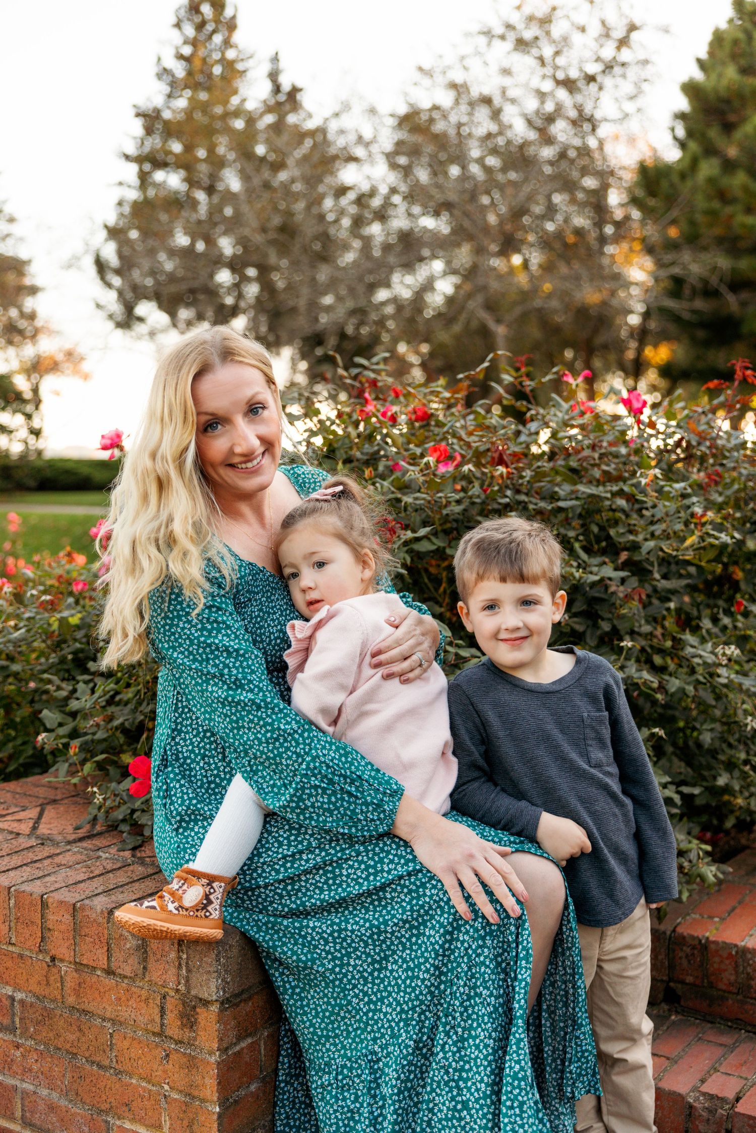 Family sitting together on a brick wall surrounded by red flowers and autumn foliage.