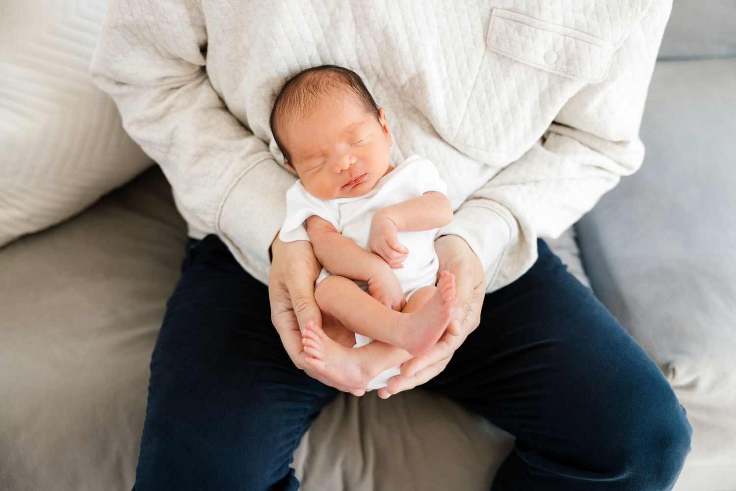 Peaceful sleeping newborn in white onesie cradled in caregiver's lap.