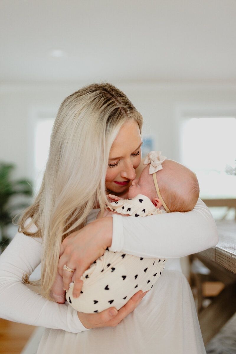 Tender moment with infant wearing heart-patterned onesie in bright home setting.