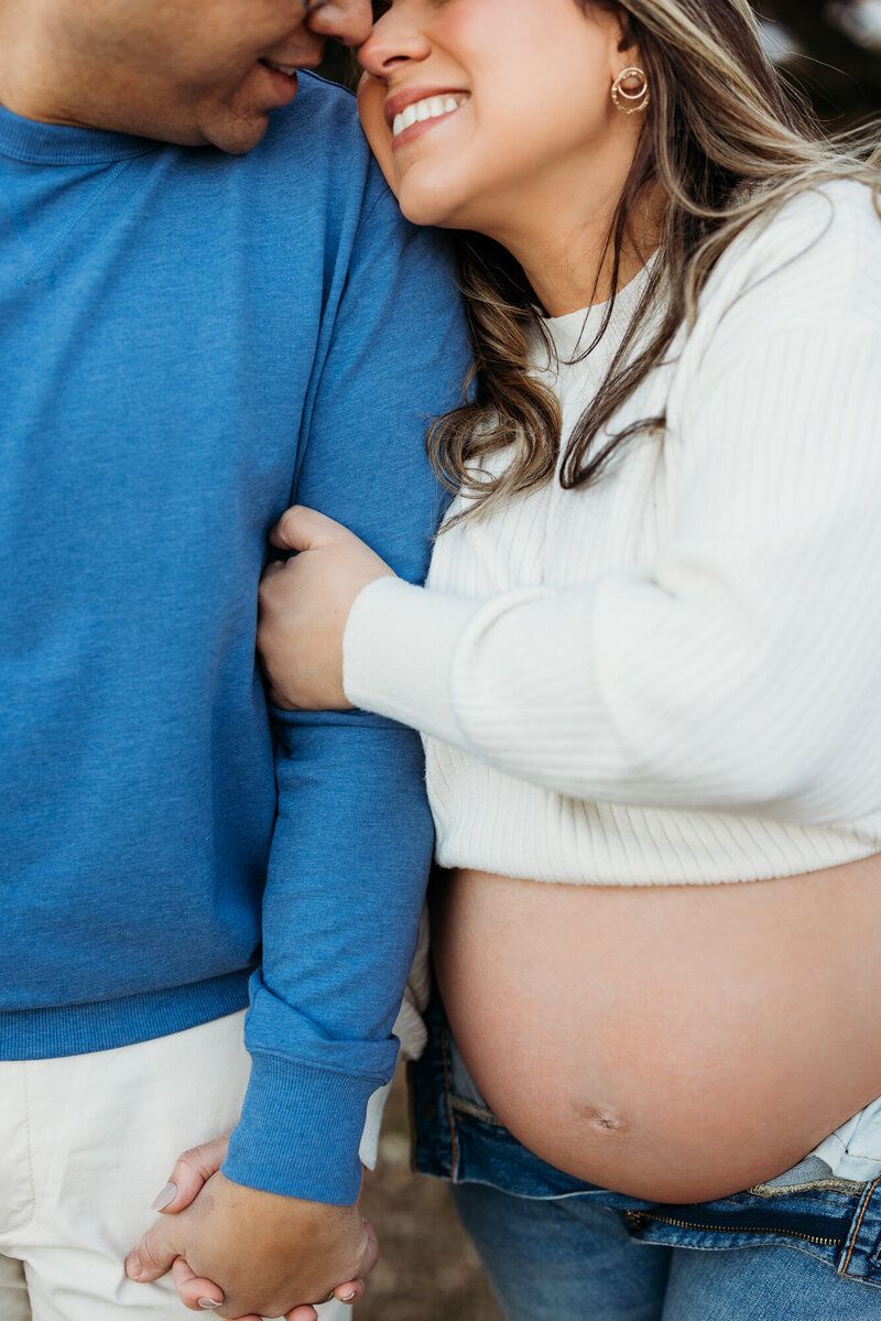 Intimate maternity portrait of couple in blue and white embracing outdoors.
