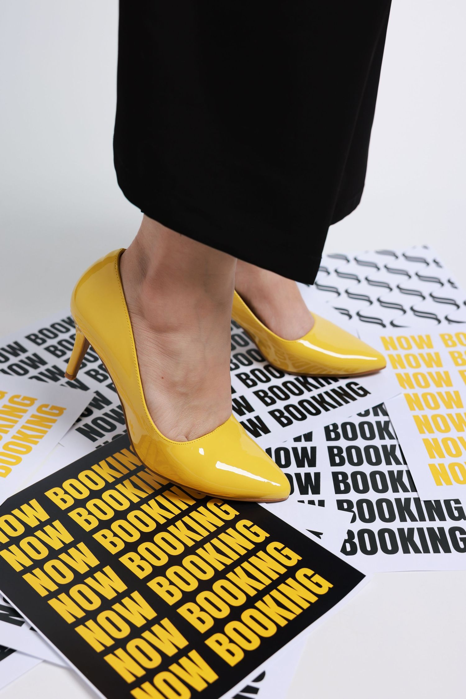 Yellow patent leather pumps step across black and yellow typography posters laid on a white surface.