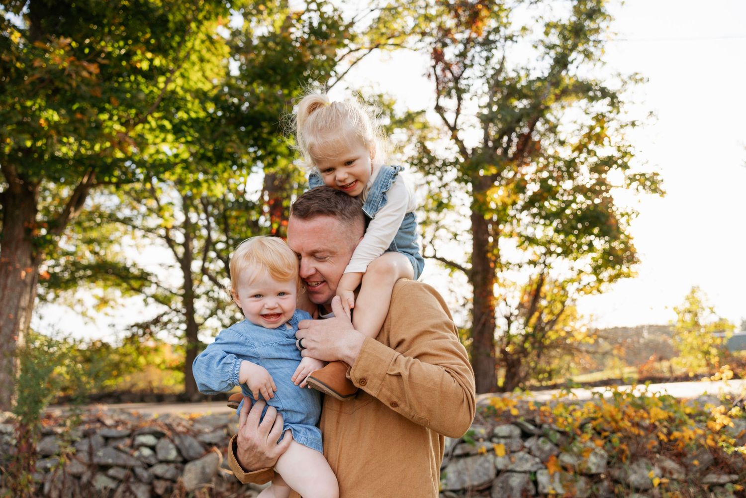 Parent and child share a tender moment together on autumn grass near a stone wall during golden hour.