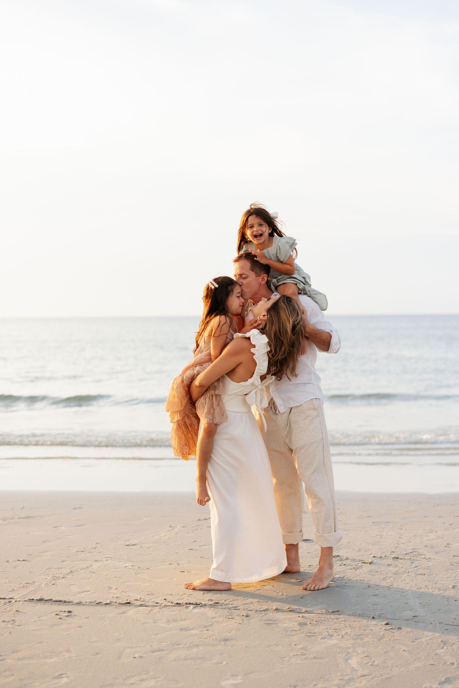 A romantic beach photoshoot captures intimate moments between a couple in white attire during golden hour.