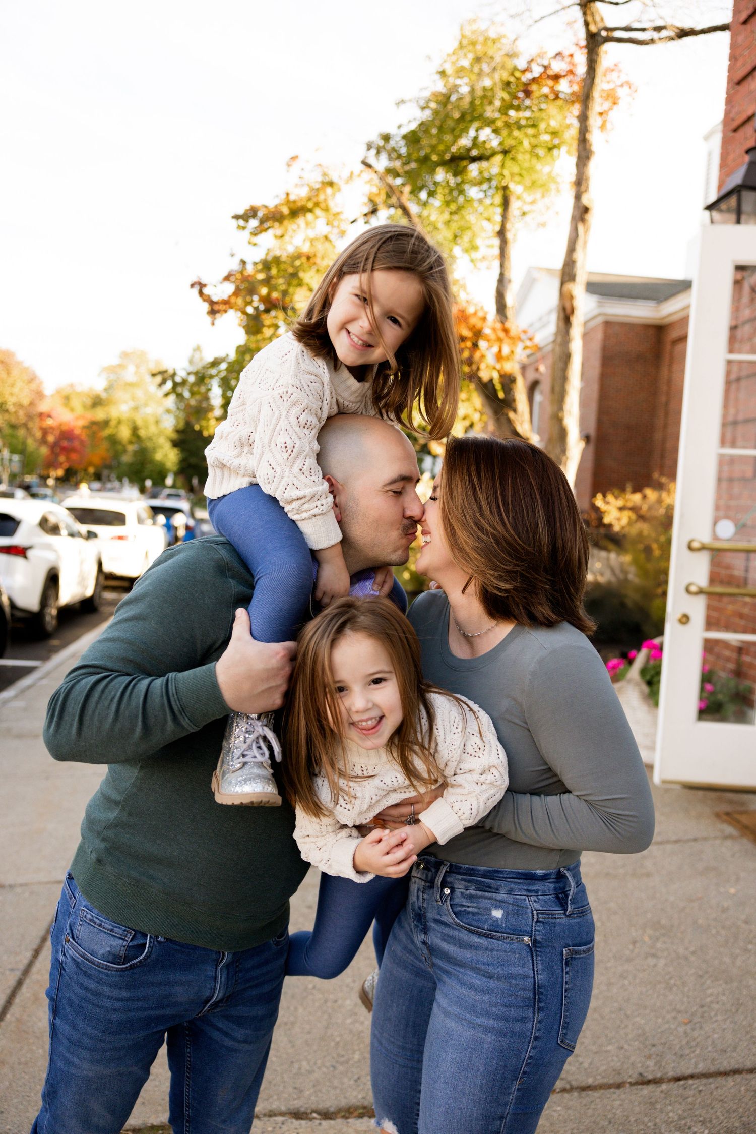 Happy family sharing playful moment together outdoors during autumn sunset near building entrance.