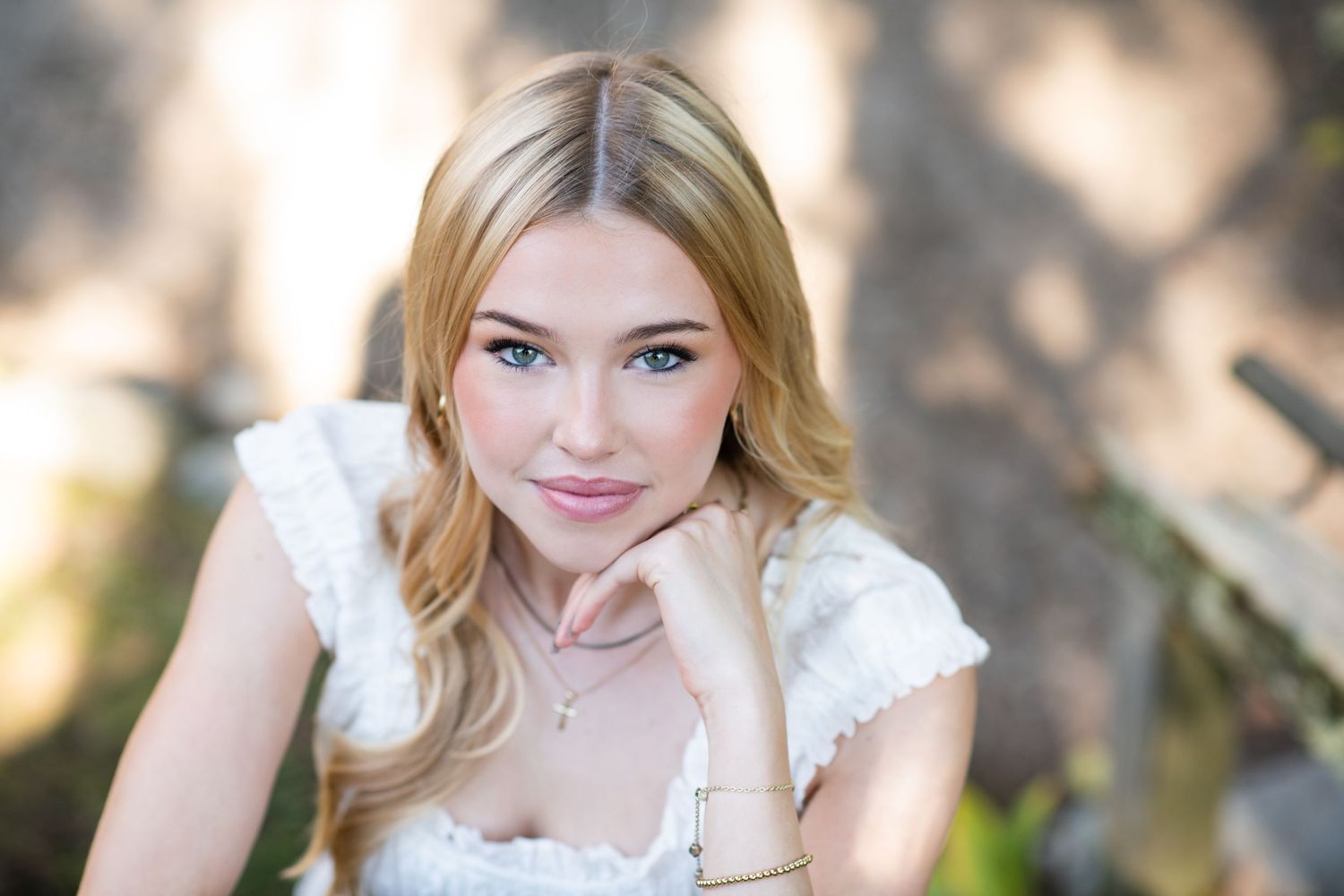 Outdoor high school senior portraits of a young woman in a light-colored dress against a natural backdrop.