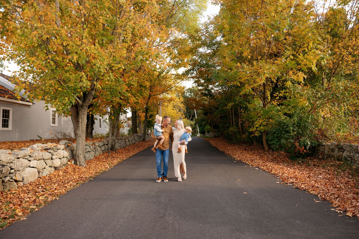 Family walking down a tree-lined path with golden fall foliage overhead on a sunny autumn day.