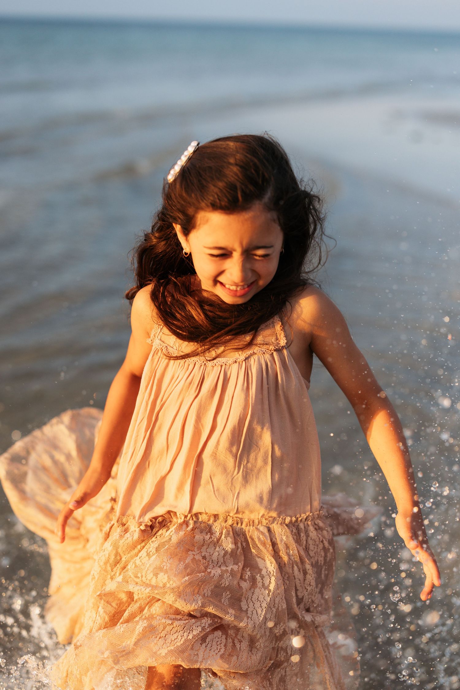 Young girl in pink dress splashes joyfully in ocean waves at the beach.