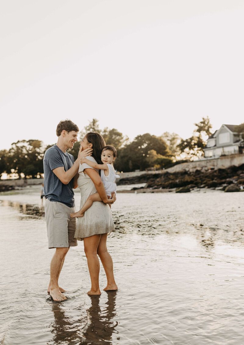 Family enjoying tender moments while standing in shallow water at sunset.