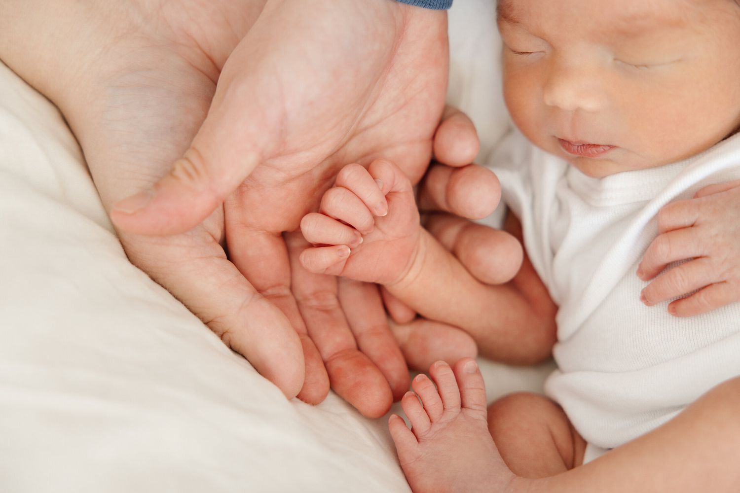 Close-up of tiny newborn hand held gently in adult hands.