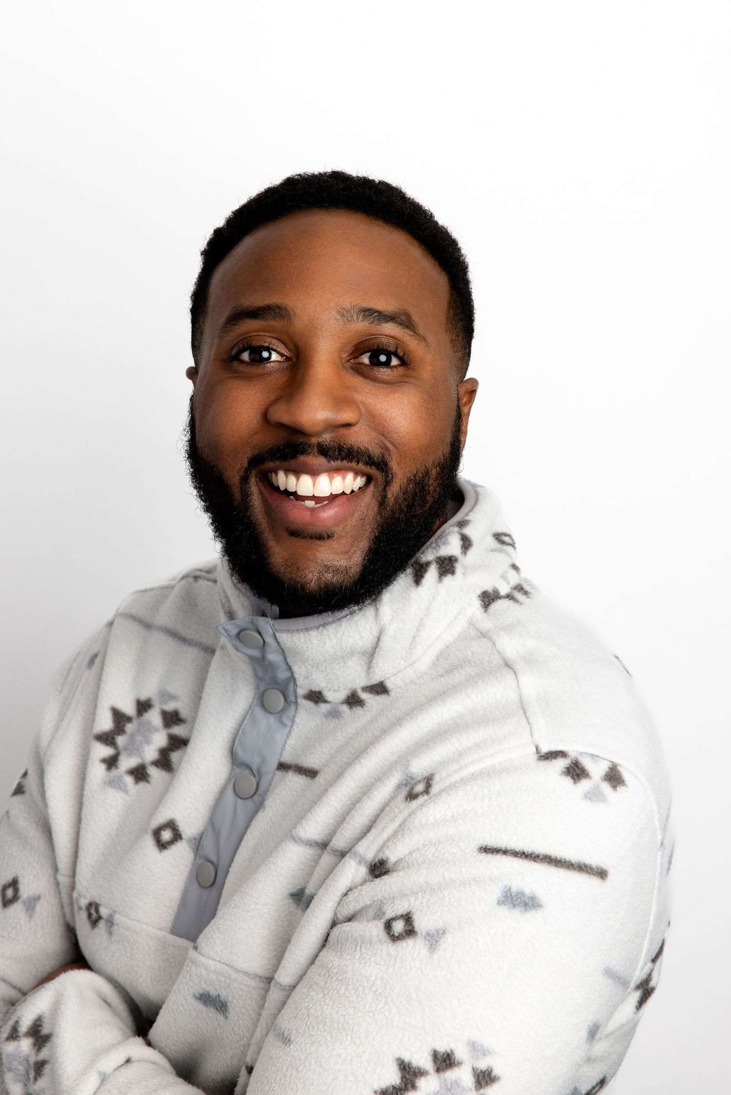 Smiling Black man with beard wearing a white Aztec print fleece pullover against a white background.