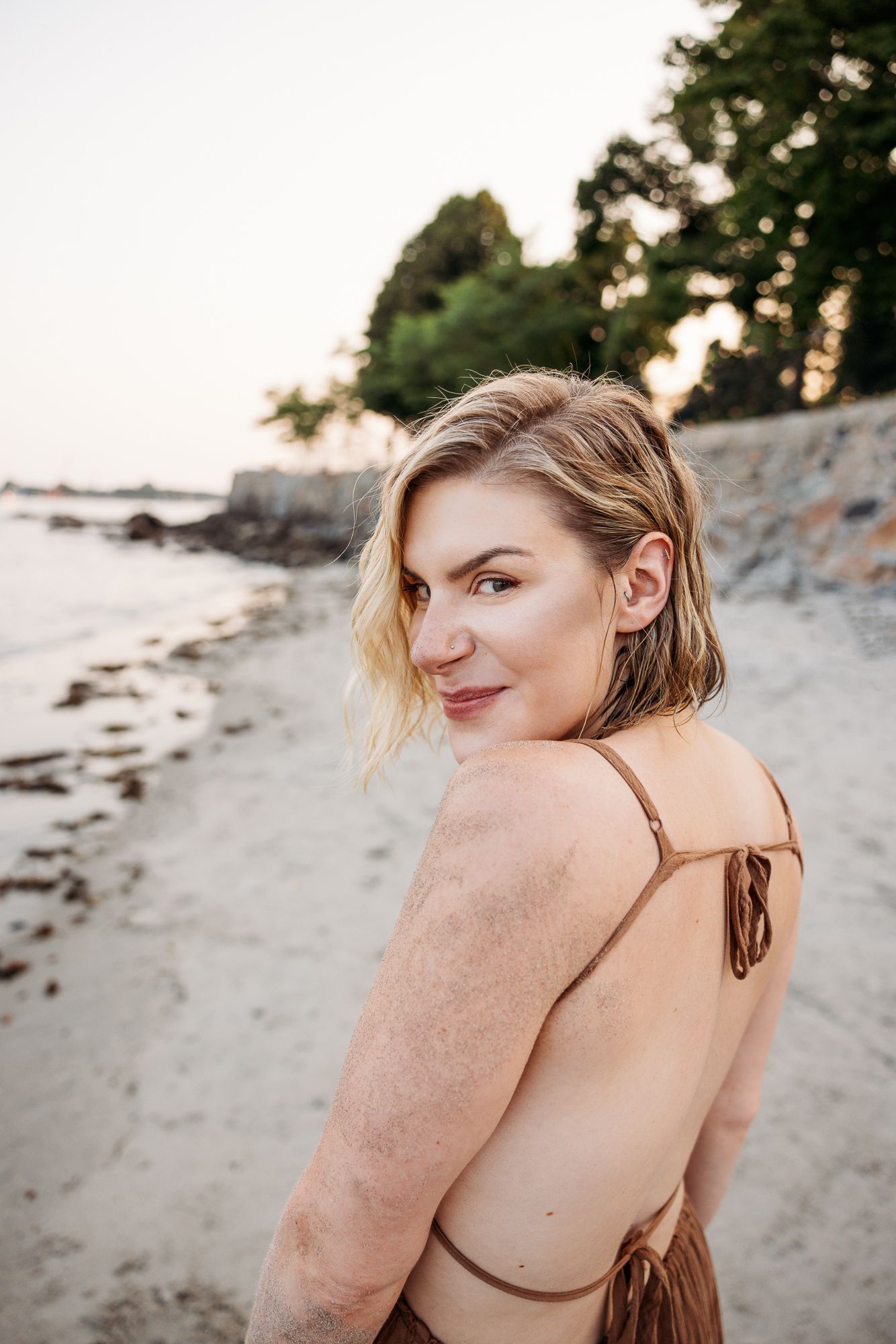 Figure in brown dress sitting on beach with natural light creating warm tones.