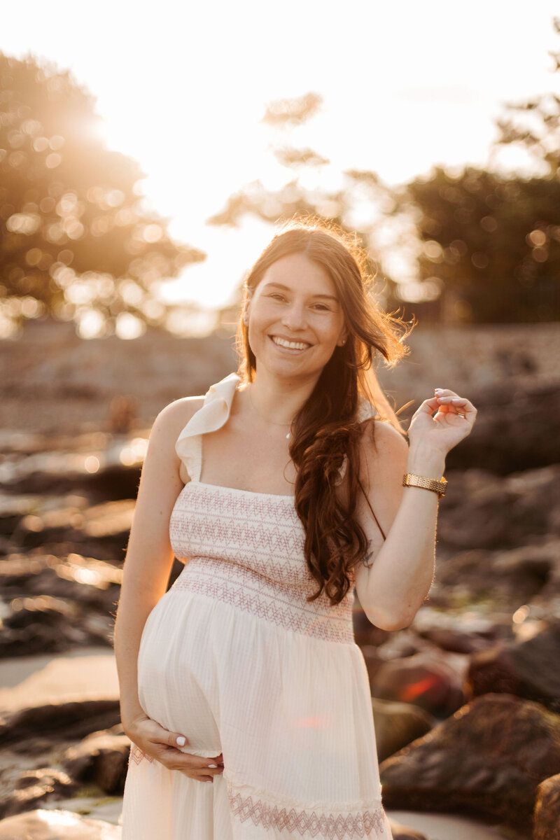 Woman in white summer dress poses playfully during golden hour sunset.