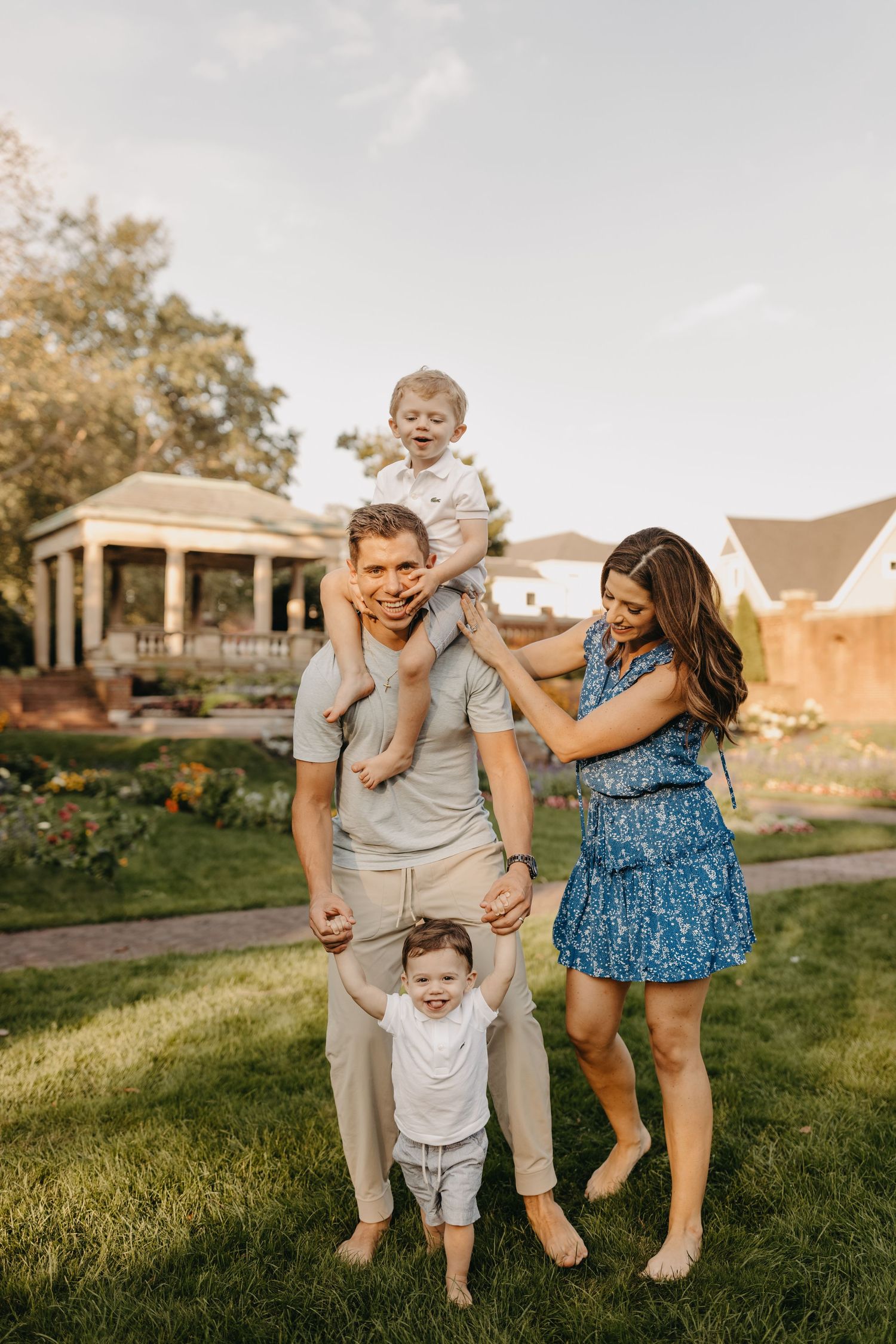 Family enjoying playful moments together on a grassy lawn during golden hour.
