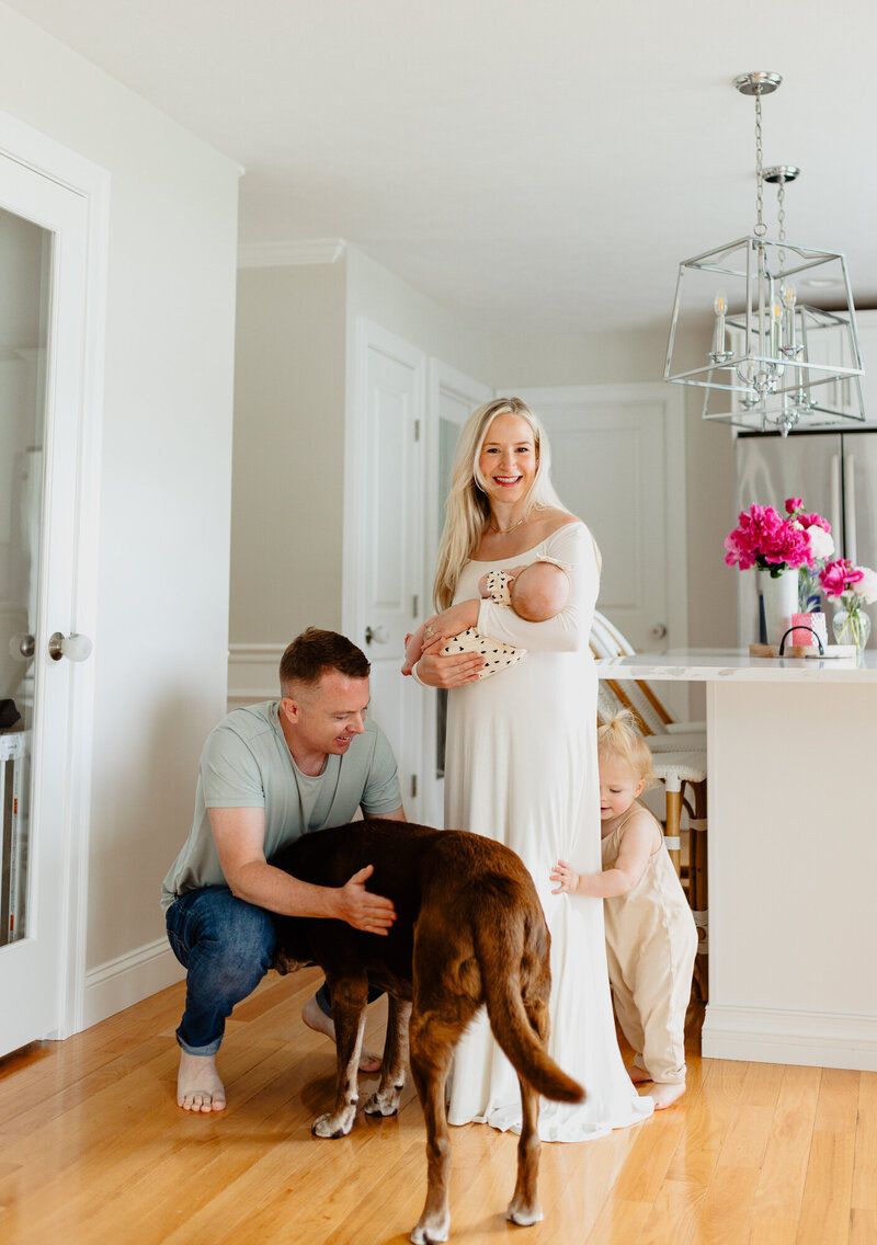 Family photoshoot showing playful interactions with a brown dog in a modern white room with hardwood floors.