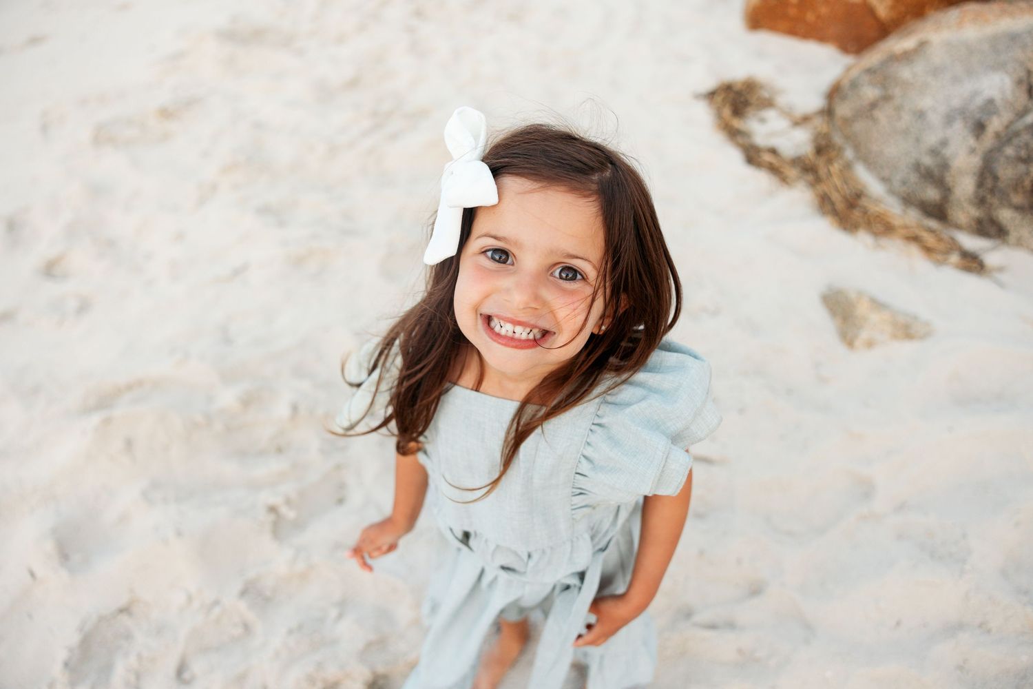 A young person joyfully runs and plays in the sand at a beach, with their hair flowing in the wind.
