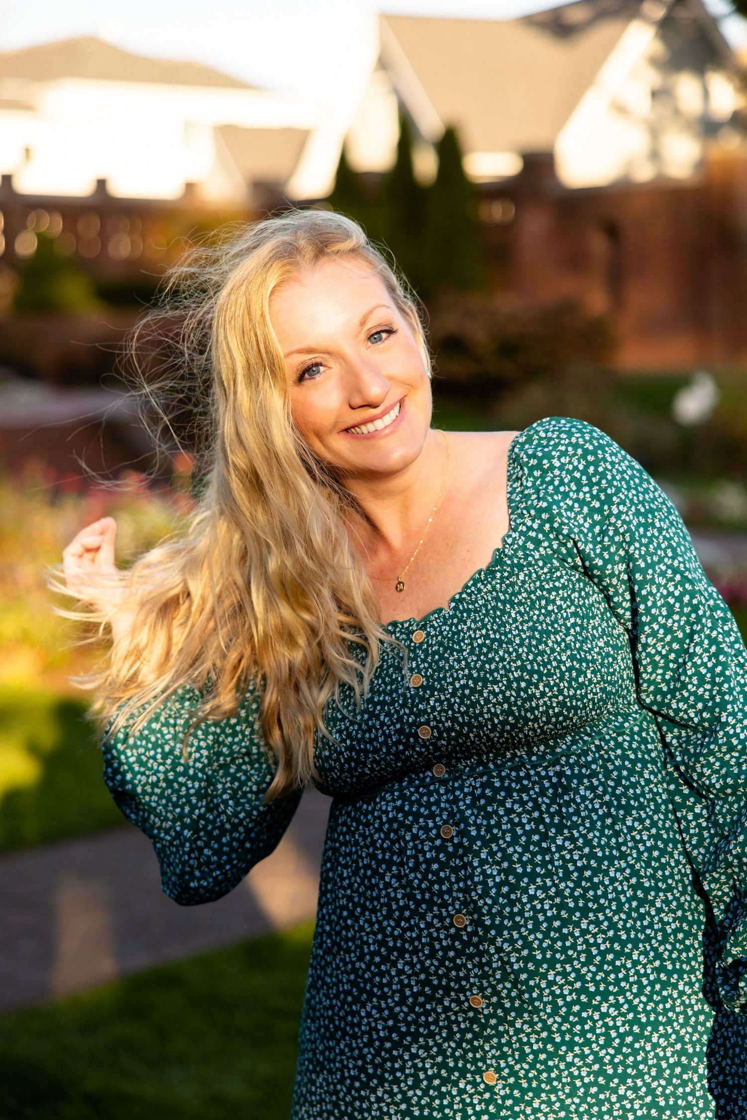 Woman in green polka dot dress spins joyfully in golden sunlight during outdoor photo session.