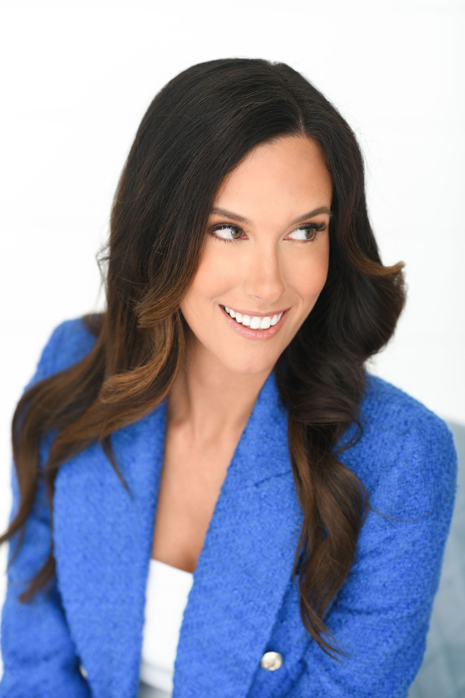 A confident woman with long dark hair wearing a blue blazer smiles against a clean white background.