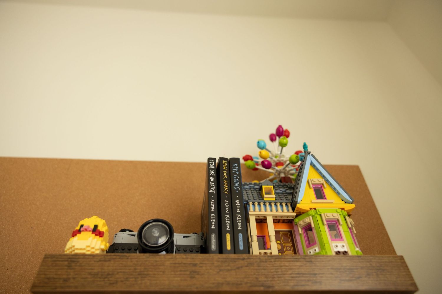 Books, toys, and various items arranged on a long wooden shelf against a beige wall.
