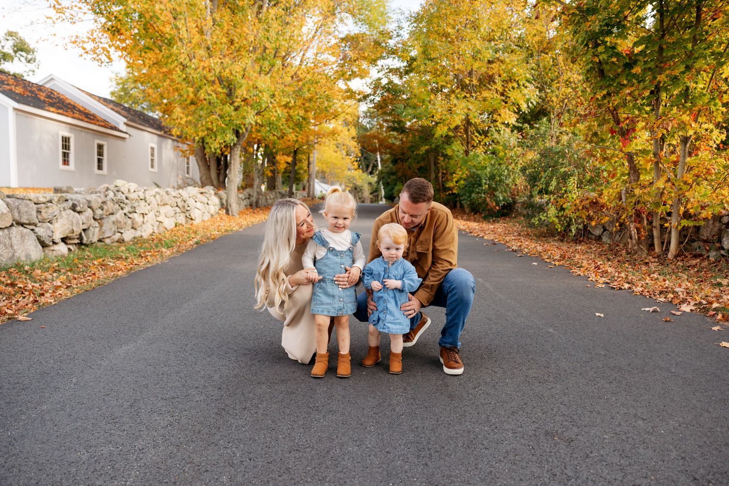A family takes autumn photos together on a tree-lined street with golden yellow foliage.