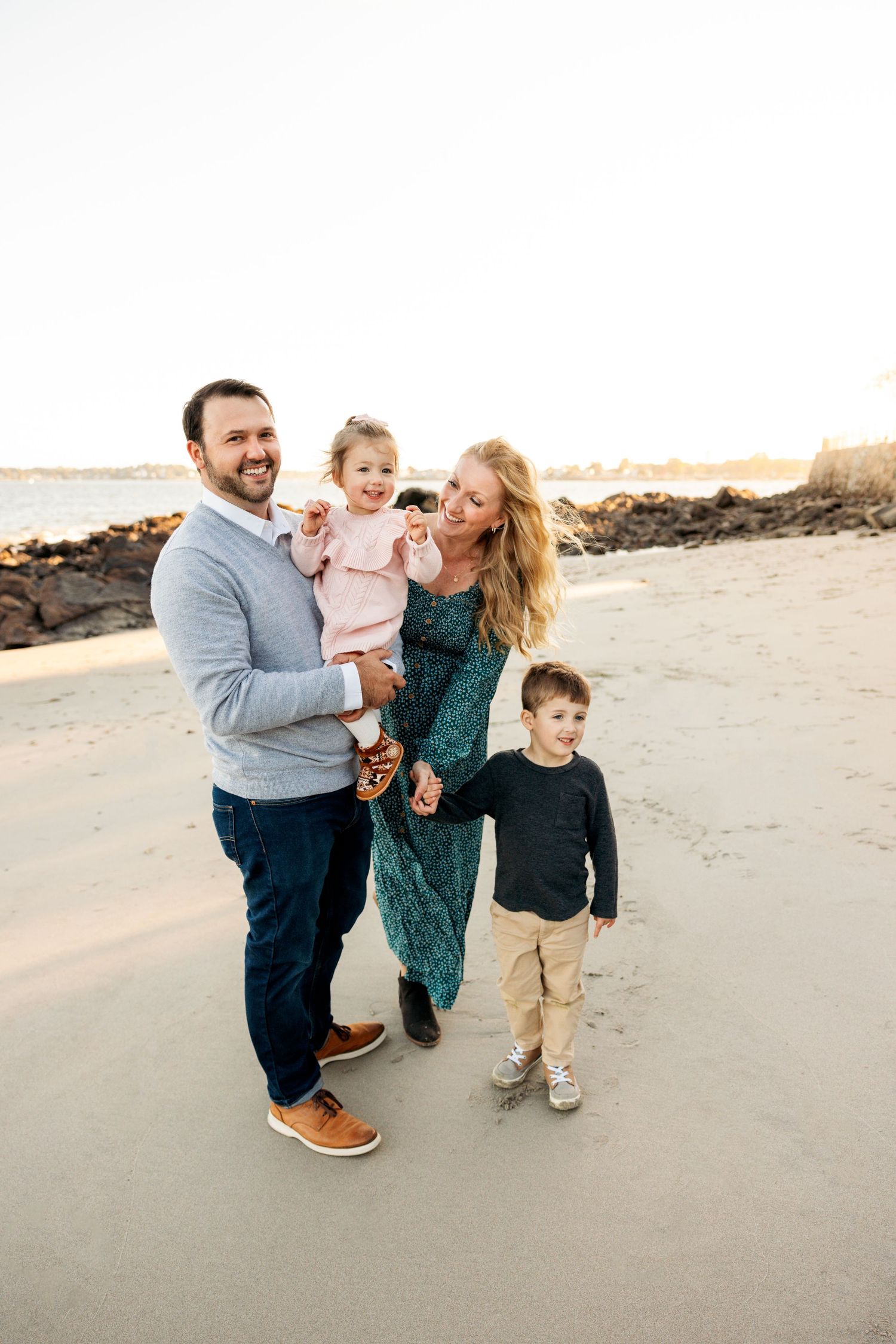 Family walking and playing together on a sandy beach during sunset with casual attire.