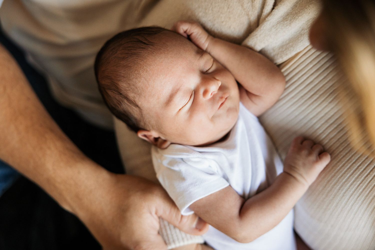 Sleeping newborn baby in white onesie resting peacefully.