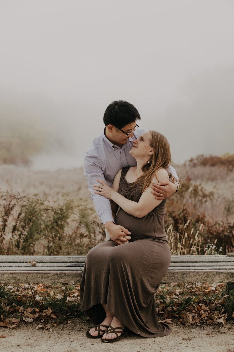 Couple shares intimate moment on wooden bench during autumn photoshoot.