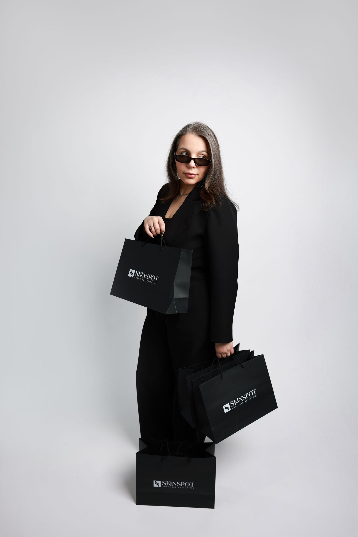 Person in black outfit holding multiple luxury shopping bags against white background.