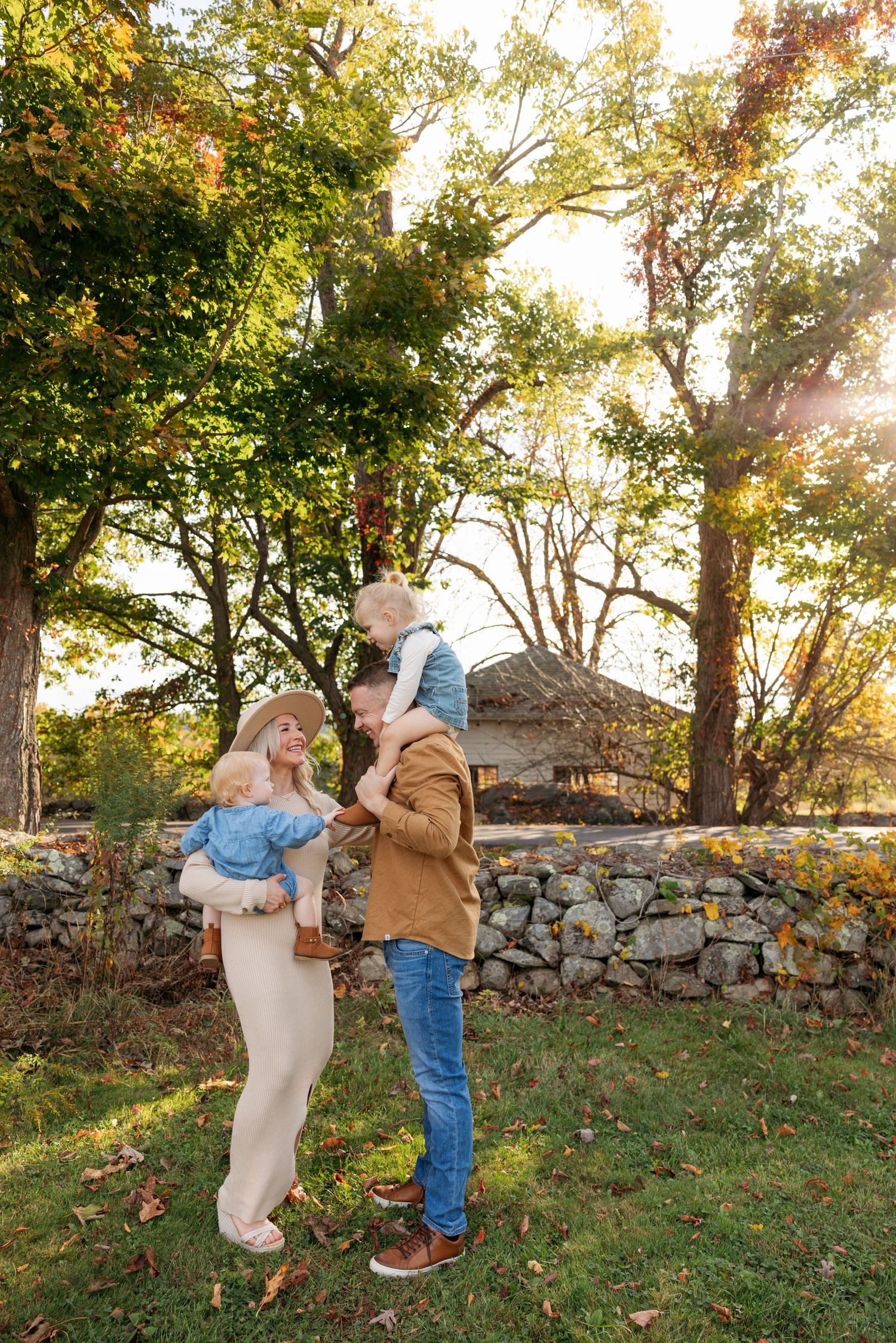 Playful family moment by stone wall surrounded by fall foliage and warm sunlight.