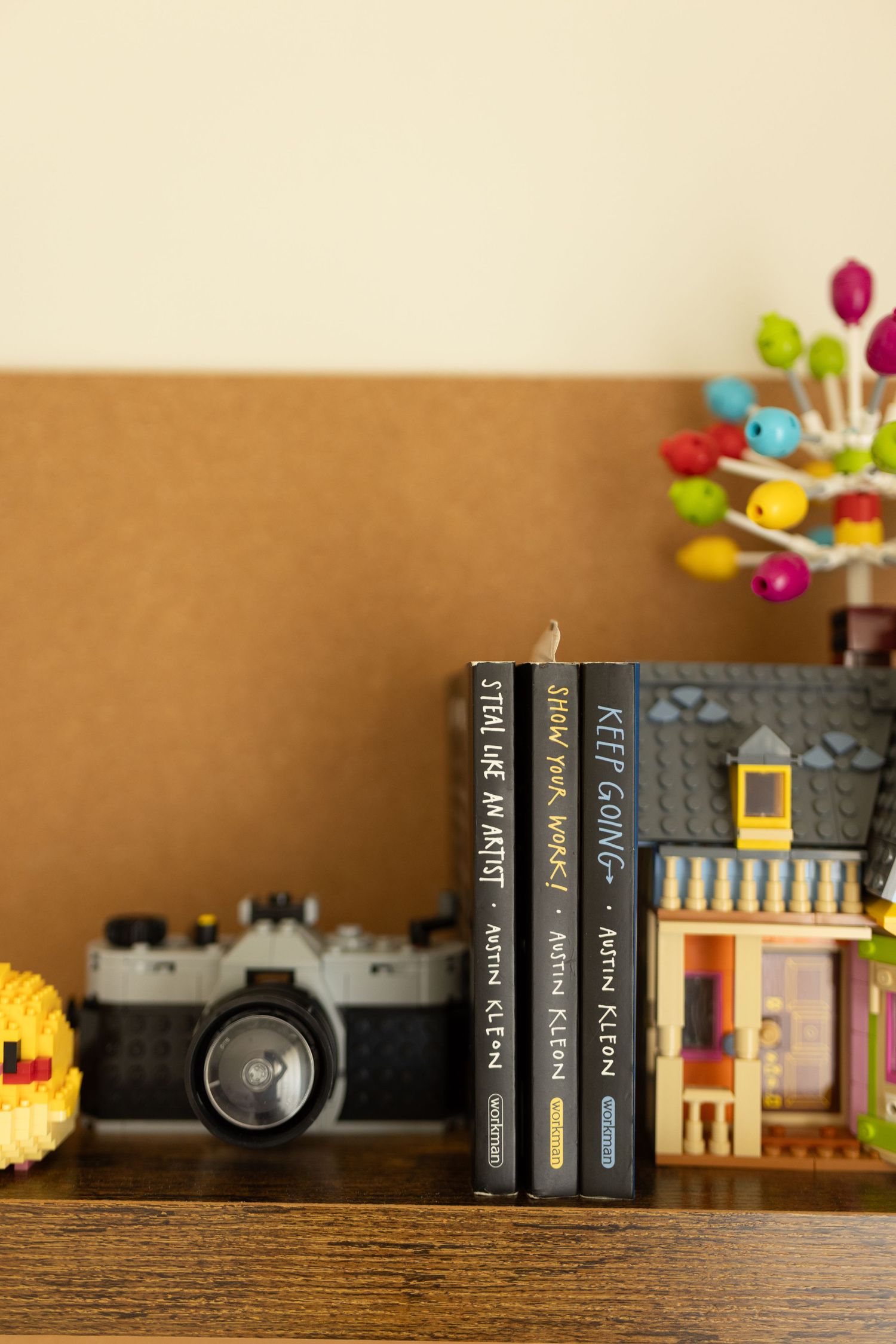 A rustic wooden shelf displays a collection of dark-colored books with colorful toys peeking over the top.