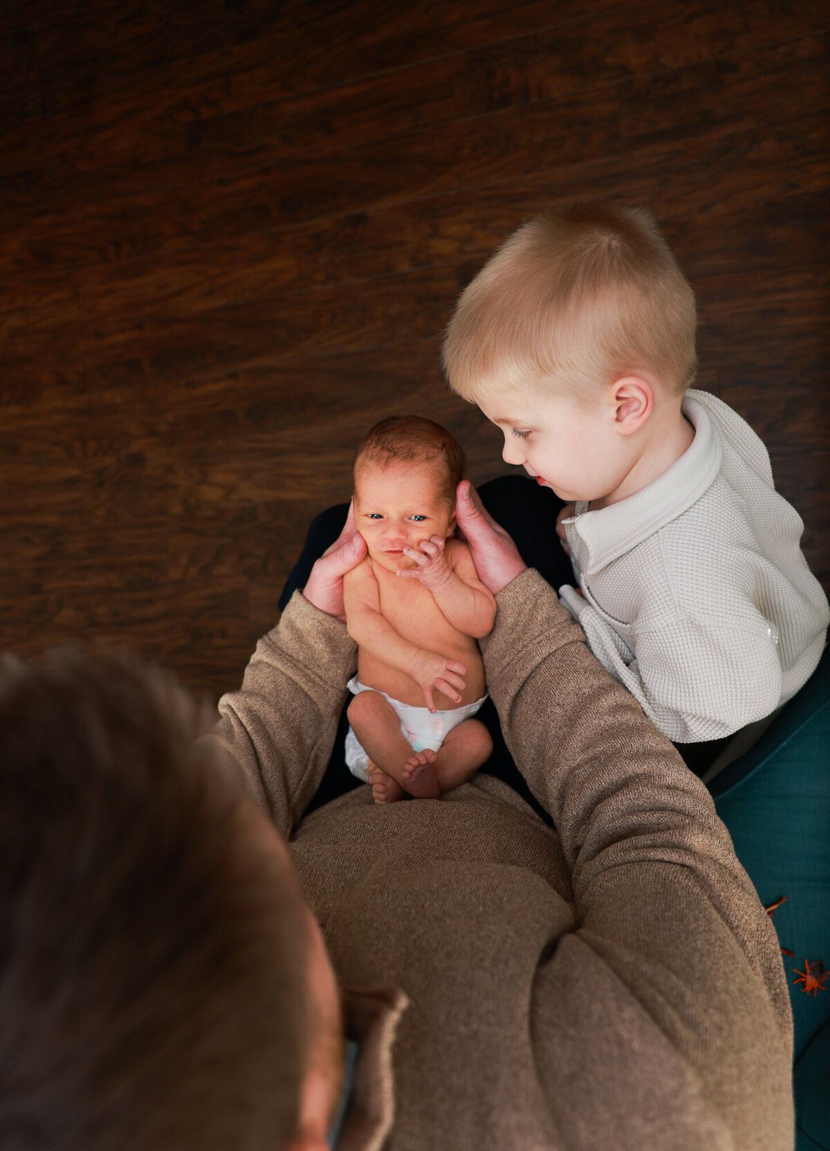 A newborn baby being held while an older sibling looks on with curiosity.