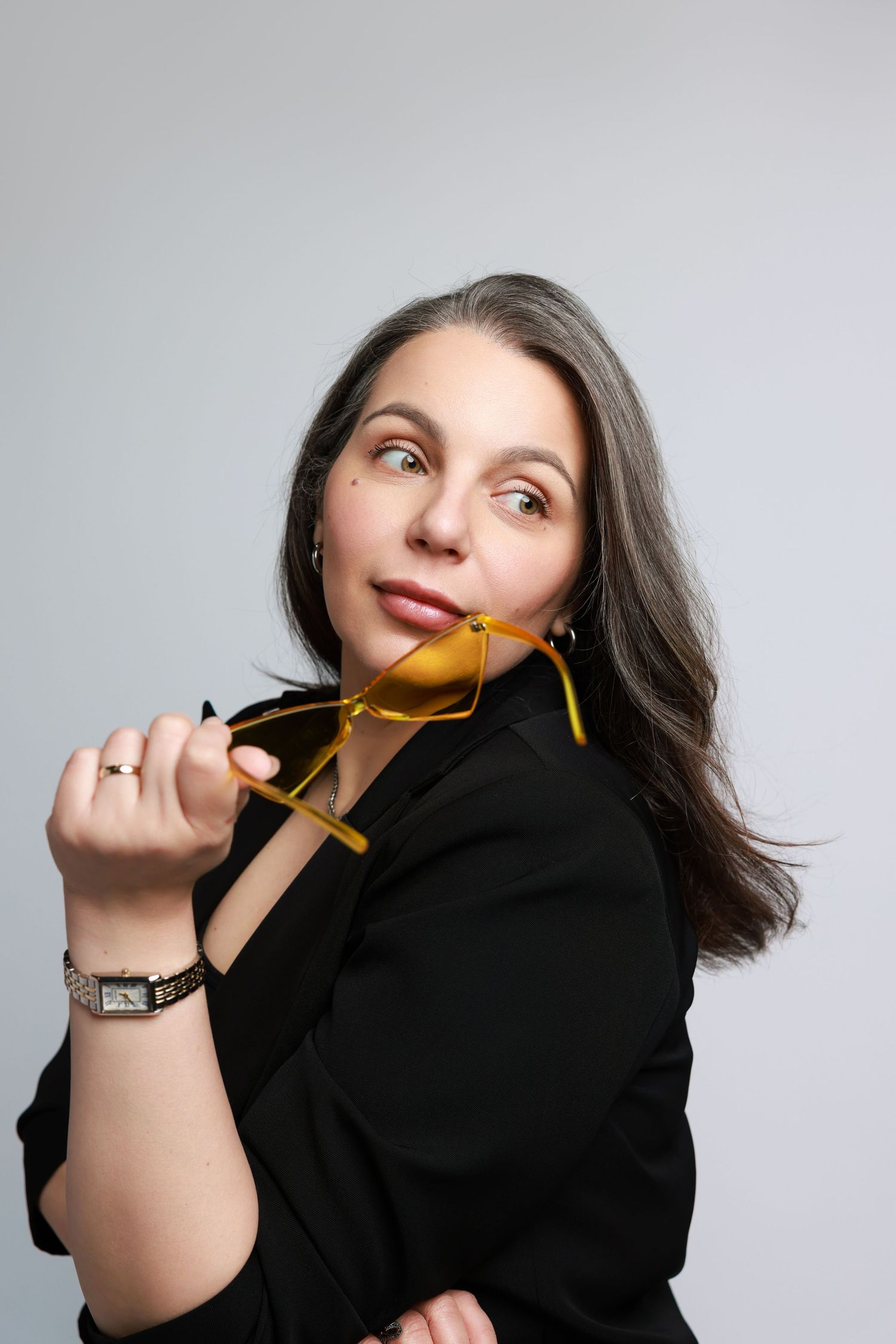 A playful portrait series against a light background showing someone with dark hair playing with orange glasses.