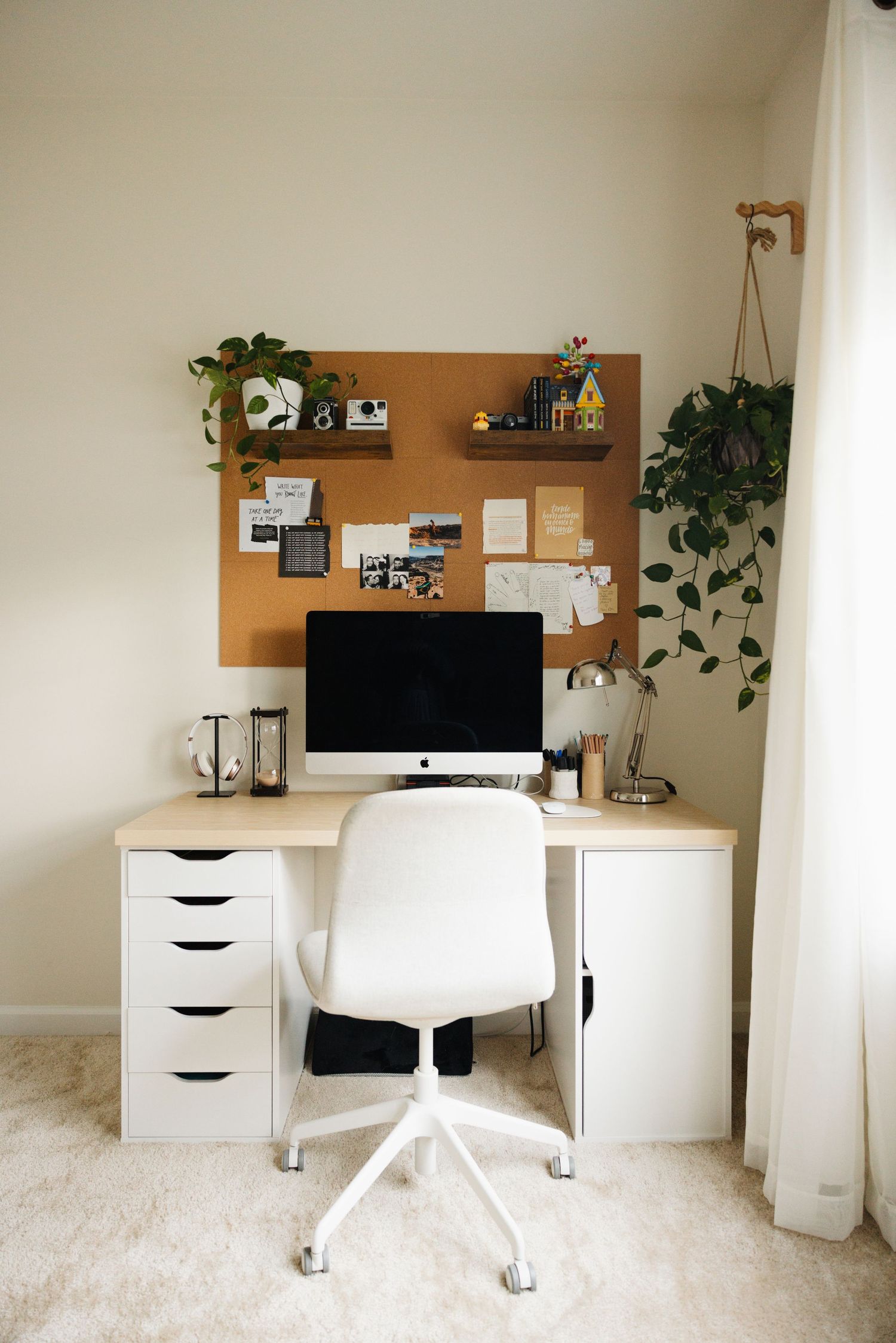 Modern minimalist home office setup with white furniture, cork board, and plants against beige walls showing room angles.