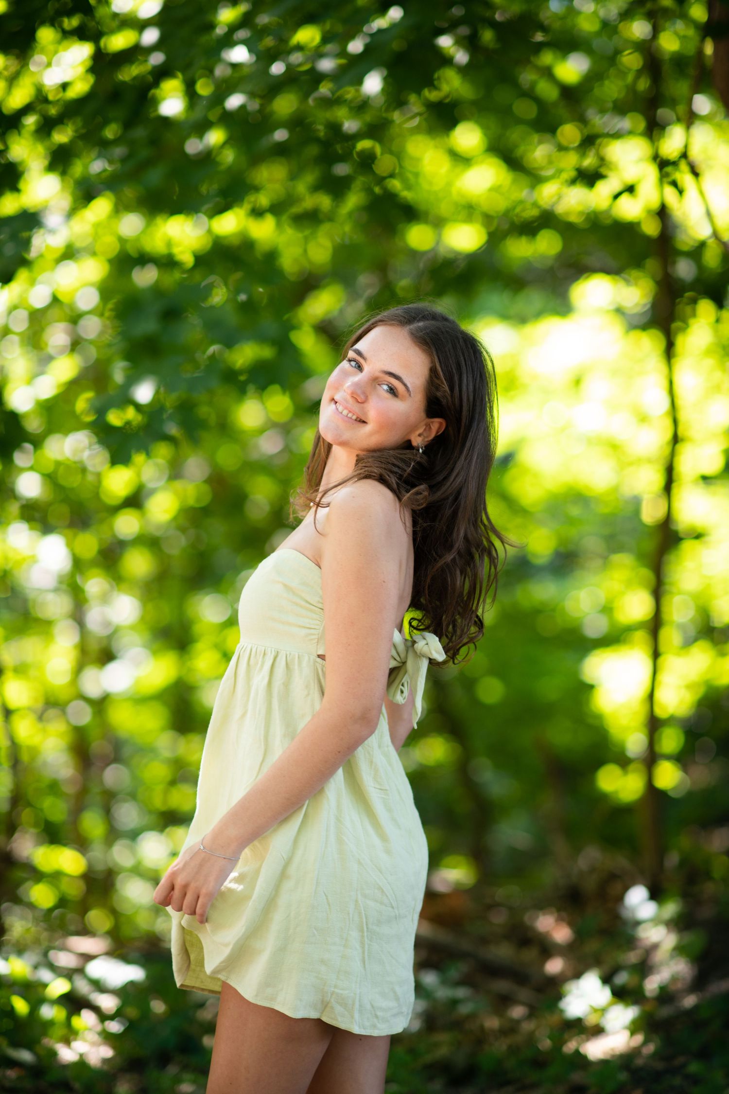 Nature portrait session in a sun-dappled forest with soft lighting and vibrant green foliage.