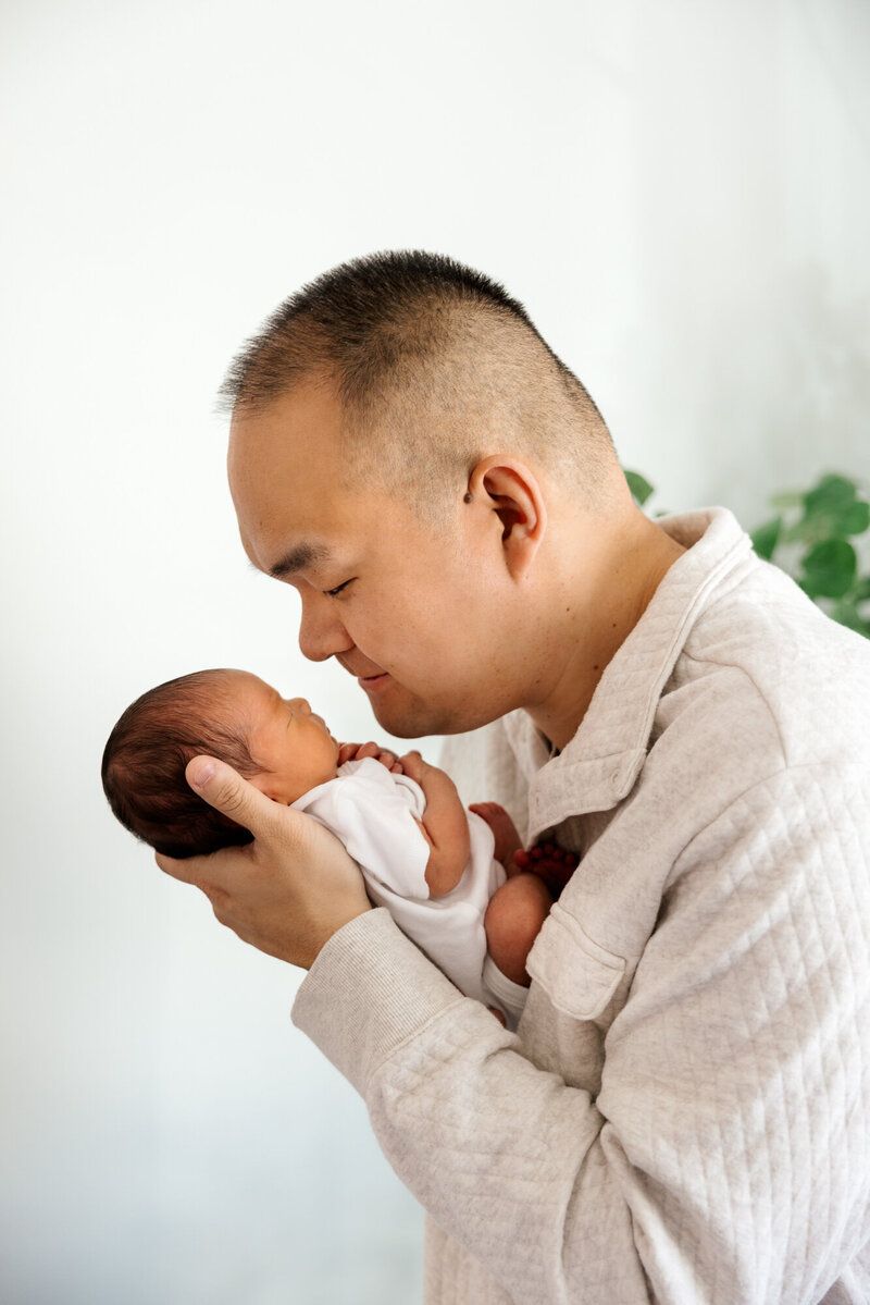 Gentle moment between parent and newborn baby in white room.