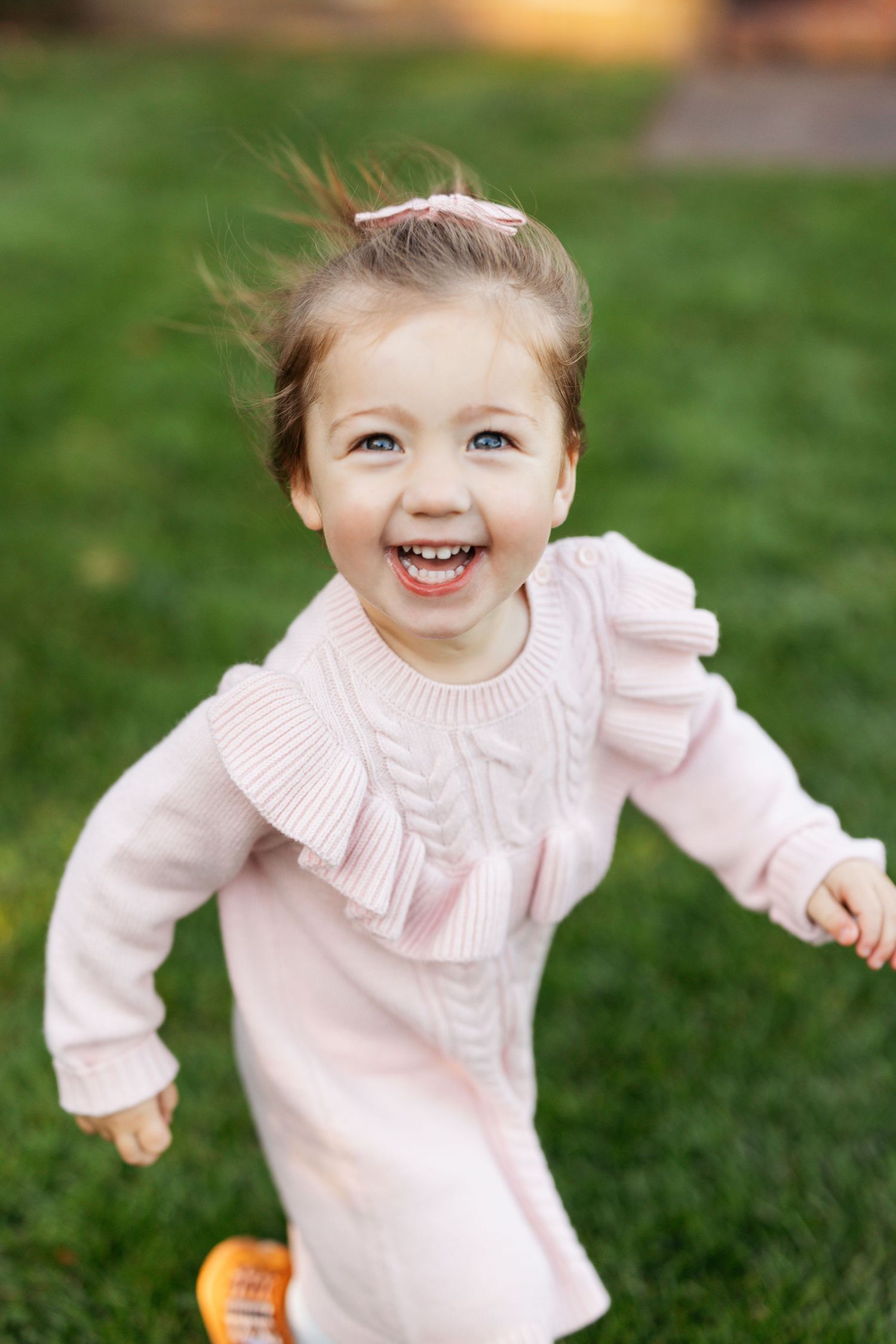 A smiling toddler wearing a pink ruffled sweater plays on green grass in a series of sweet expressions.