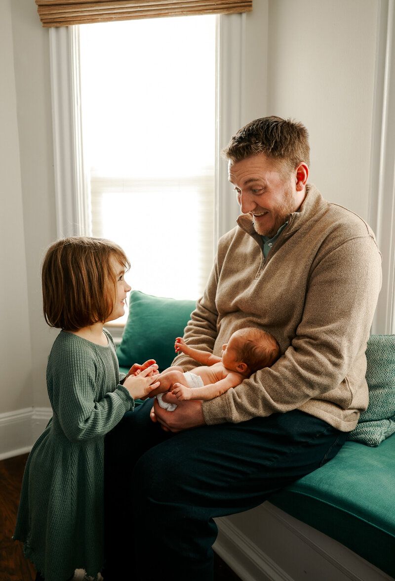 Family members share intimate moments while seated on a dark green couch in a sunlit room.