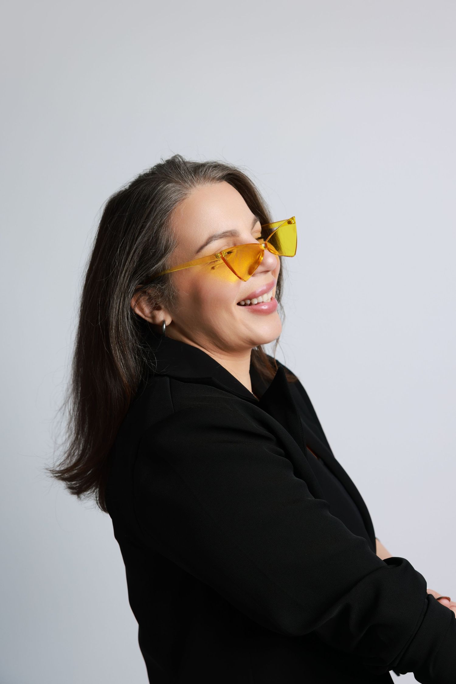 A person wearing a black turtleneck holds a yellow flower playfully against their nose in a minimalist studio setting.