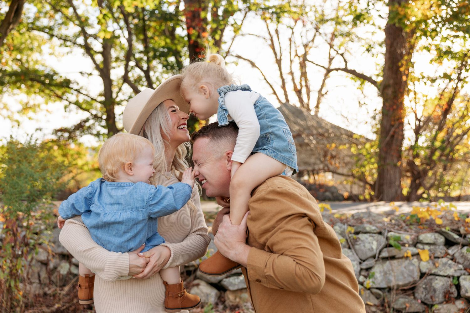 Two people share a romantic embrace against a rustic stone wall during golden hour lighting.