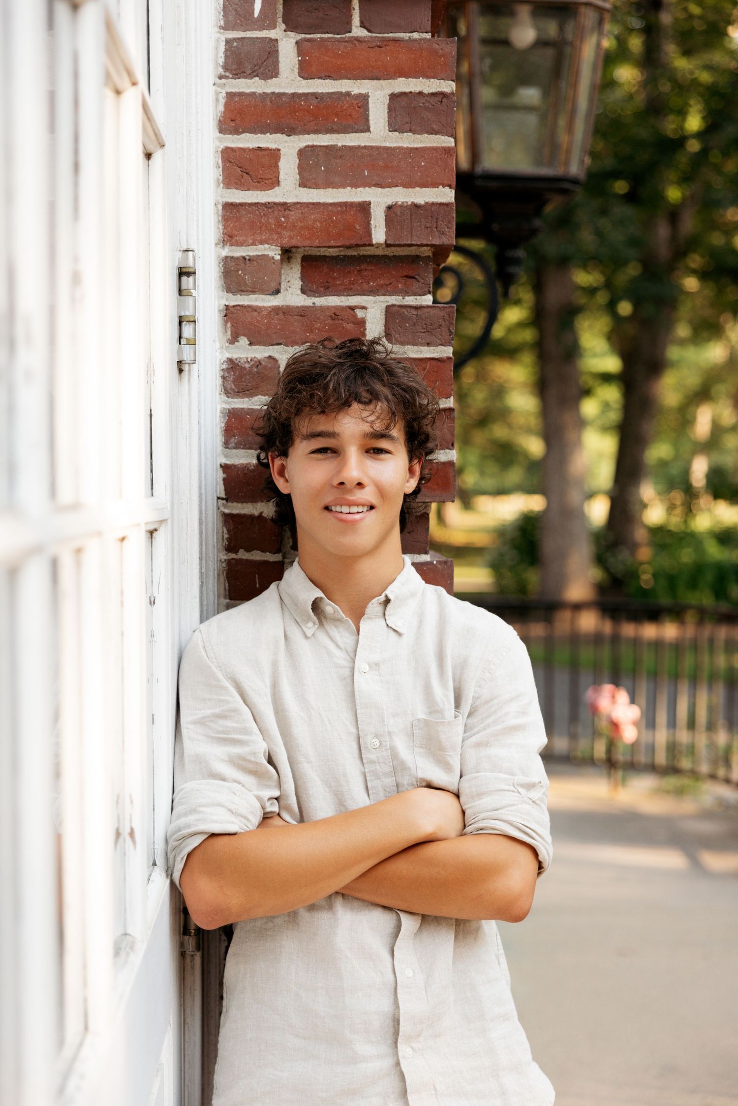 Person in a white shirt poses against a red brick wall with white columns on a sunny day.
