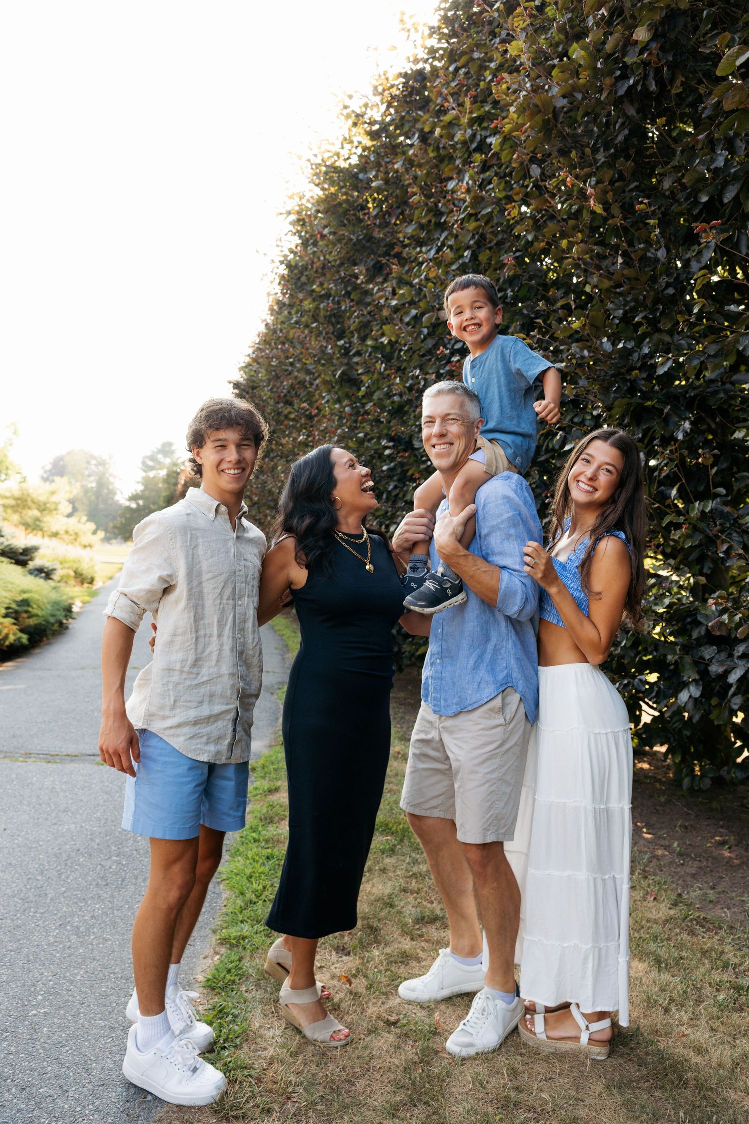 A group laughs together during a casual outdoor photo session on a paved path.